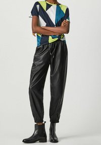 T-shirt z wielokolorowym geometrycznym nadrukiem z bawełny; czarne dresy z sztucznej skóry z elastycznymi mankietami; czarne botki za kostkę z teksturowanym wykończeniem.