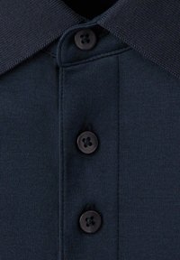 Polo bleu marine foncé en gros plan montrant le col et trois boutons noirs sur la patte de boutonnage.