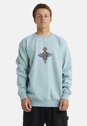 Light blue sweatshirt made of cotton, featuring an embroidered design in orange and black at the center. Ribbed cuffs and hem.