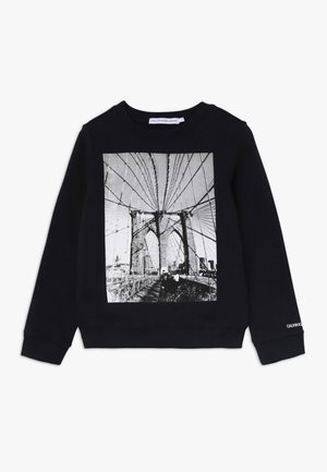 Musta pitkähihainen collegepaita, jossa mustavalkoinen grafiikka Brooklynin sillan kaapeleista ja tornista edessä, pieni valkoinen logo hihansuun kohdalla.