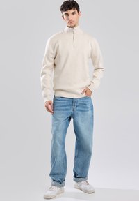 Beige zip-neck sweater, soft texture, paired with light blue denim jeans, relaxed fit, and white sneakers. Simple and versatile outfit.