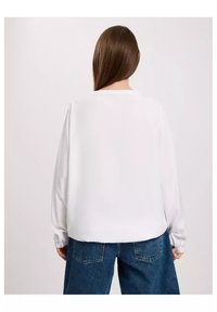 Biała koszula z długim rękawem, okrągłym dekoltem i luźnym krojem, w zestawieniu z dżinsami w kolorze niebieskim i wysokim stanem. Miękka struktura, minimalistyczny design.