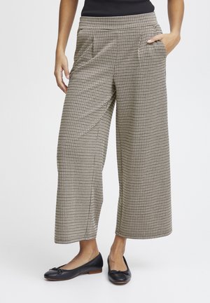 Weite Hosen im schwarz-beigen Karomuster, mit seitlichen Taschen und einer glatten Textur. Kombiniert mit schwarzen Ballerinas.