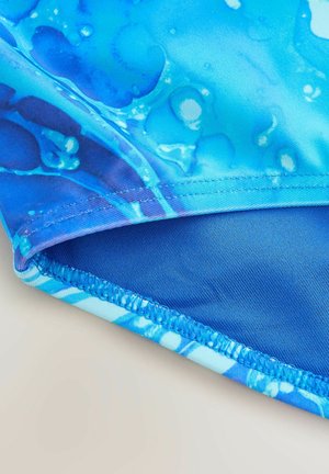 Detailný záber modrej látky so vzorom kvapiek vody a precíznym prešívaním pozdĺž okraja švu.