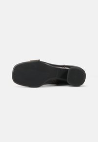 Suela de zapato de cuero negro con un acabado suave, agarre texturizado y una ligera curvatura. Presenta un pequeño acento marrón en el lateral.