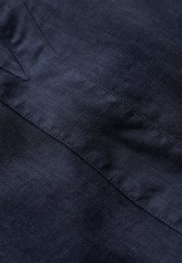 Marineblauwe linnen stof met een gladde textuur, subtiele glans en versterkte stiksels. Het materiaal lijkt lichtgewicht en ademend te zijn.