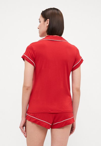 Red short-sleeved pajama top with white piping and matching shorts. Soft fabric, relaxed fit, and side ruffle detail on shorts.