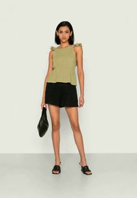 Top sem mangas verde oliva com alças fru-fru, combinado com calções pretos e acessórios pretos. Tecido suave com um corte descontraído.