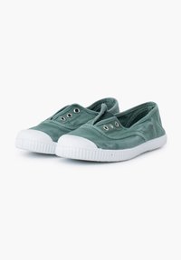 Las zapatillas de lona verde tipo slip-on presentan una puntera redonda de goma blanca y ojales de metal para ventilación. Suela plana con agarre texturizado.