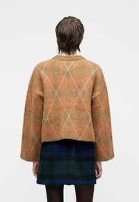 Pull oversized court en orange et beige avec un motif en losange, conçu en tricot doux. Associé à une jupe à carreaux bleue.