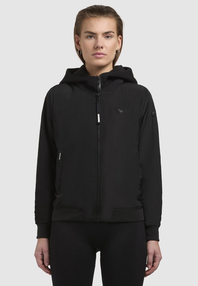 Veste à capuche zippée noire avec des manches raglan, dotée d'une texture douce, de poignets élastiques et d'un petit logo sur la poitrine.