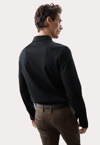 Schwarzes Langarmhemd mit Kentkragen, glatter Textur und tailliertem Schnitt, kombiniert mit braunen Hosen und einem schwarzen Gürtel.