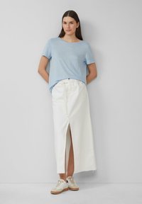 Lichtblauw T-shirt met korte mouwen, gecombineerd met een lange witte spijkerrok voorzien van een voorlits, aangevuld met witte sneakers met bruine accenten.