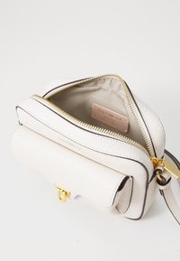 White textured leather crossbody bag with gold hardware, double zip closure, and a front pocket. Inside features a smooth lining and brand tag.