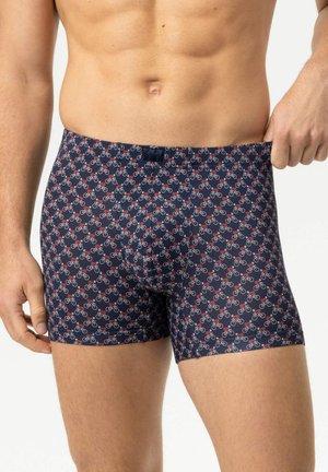 Mann trägt dunkelblaue Boxershorts mit einem roten und weißen Fahrradmuster und zieht den Bund leicht nach außen.