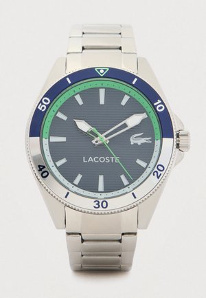 Reloj de acero inoxidable plateado con una esfera gris oscuro, acentos verdes y azules, y un logo de cocodrilo. Presenta un bisel numérico y manecillas luminosas.