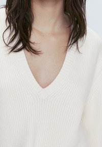 Pull en laine crème à col en V avec texture côtelée. Doté d'une coupe ample et d'un motif texturé sur le tissu. Pas de matériel ou d'accents notables.