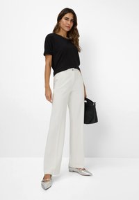 Zwart T-shirt met korte mouwen gecombineerd met witte wijde broek, zilveren flats en een zwarte geweven handtas. Gladde texturen en een eenvoudig ontwerp.