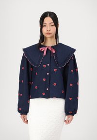 Ναυτικό τζάκετ από τζιν με μεγάλο φουσκωτό γιακά, ροζ κορδέλα και κεντημένη κόκκινη καρδιά. Έχει κλείσιμο με κουμπιά και φουσκωτά μανίκια.