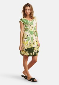 Floral dress featuring green and yellow leaf patterns, v-neckline, short sleeves, cinched waist with a tie belt, and a loose fit.