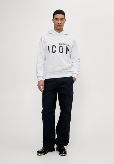 Sweatshirt à capuche blanche avec "ICON" en texte noir, associé à un pantalon cargo bleu marine foncé et des chaussures noires avec des accents métalliques.
