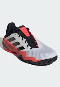 Weißer und roter synthetischer Sportschuh mit strukturiertem Obermaterial, schwarzen Akzenten und einer Gummisohle mit Zickzackmuster.