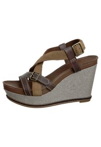 Sandale compensée marron et beige avec des brides croisées, une semelle intermédiaire en tissu gris texturé, et un détail de boucle. La hauteur de la plateforme améliore le confort.