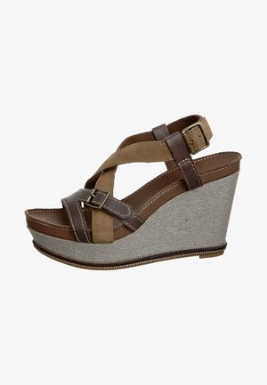 Sandale compensée marron et beige avec des brides croisées, une semelle intermédiaire en tissu gris texturé, et un détail de boucle. La hauteur de la plateforme améliore le confort.