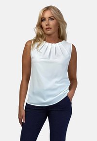 Biała bezrękawnik z plisowanym dekoltem, połączona z granatowymi spodniami w kropki. Gładki materiał o dopasowanym kroju.