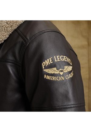 Črna usnjena jakna z ramo in bež sherpa ovratnikom ter z zlatim vezenim napisom "PME Legend American Classic" in emblemom s krili.