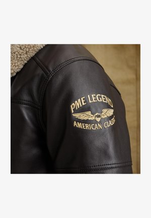 Črna usnjena jakna z ramo in bež sherpa ovratnikom ter z zlatim vezenim napisom "PME Legend American Classic" in emblemom s krili.