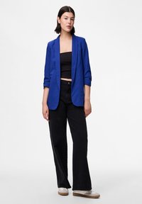 Modrý blazer s klopou, v kombinaci s černým cropped topem a černými širokými kalhotami s vysokým pasem. Neformální bílé tenisky.