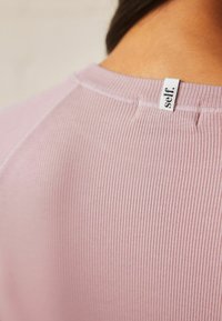 Ribad pink kangas, millel on ümmargune kaelus ja väike valge silt seljal, millel on silt "self." Sujuv tekstuur ja keha järgi istuv disain.