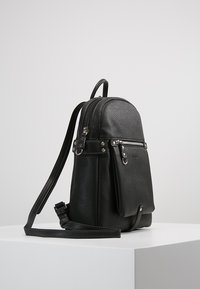 Sac à dos en cuir noir avec une finition texturée, forme incurvée, poche zippée à l'avant et bandoulière réglable. Accents en métal argenté.