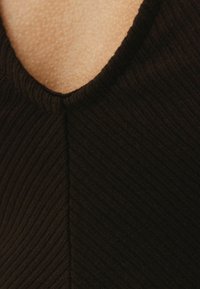 Svart ribbad tyg med V-ringning och jämn textur, med en söm ner i mitten.