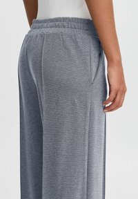 Joggers en maille grise avec une taille élastique, des poches latérales et un motif texturé, offrant une coupe ample et un design fuselé.