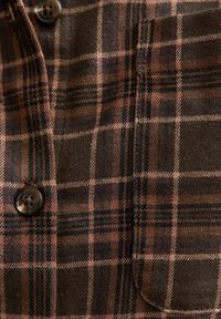Camicia a quadri marrone con tessuto testurizzato, contrasti di motivi a quadri marroni scuri e beige, e chiusura a bottoni con design a quattro fori.
