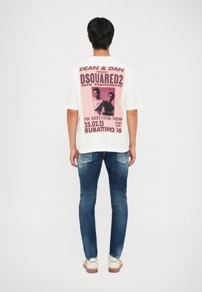 T-shirt bianco a maniche corte con una grande grafica rosa sul retro accompagnata da del testo. Jeans blu con una texture consumata e leggere rotture.