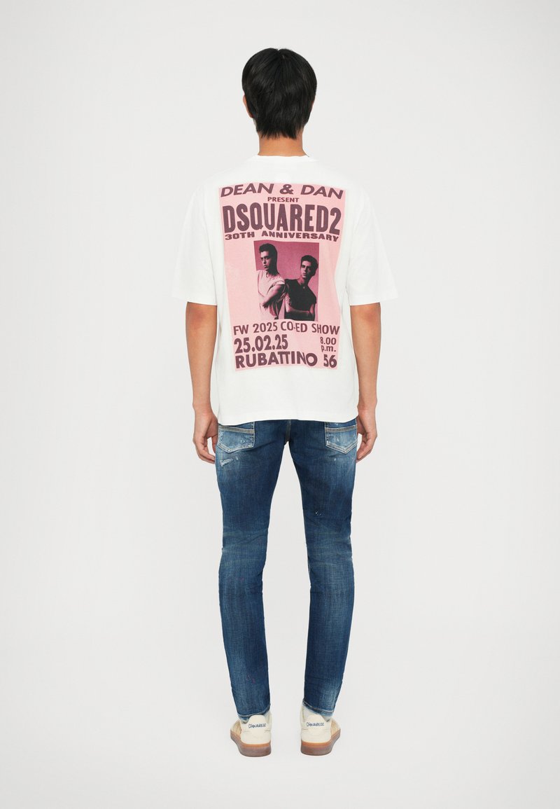 Camiseta blanca de manga corta con un gran gráfico rosa en la parte posterior y texto. Pantalones vaqueros azul con una textura desgastada y ligeras imperfecciones.