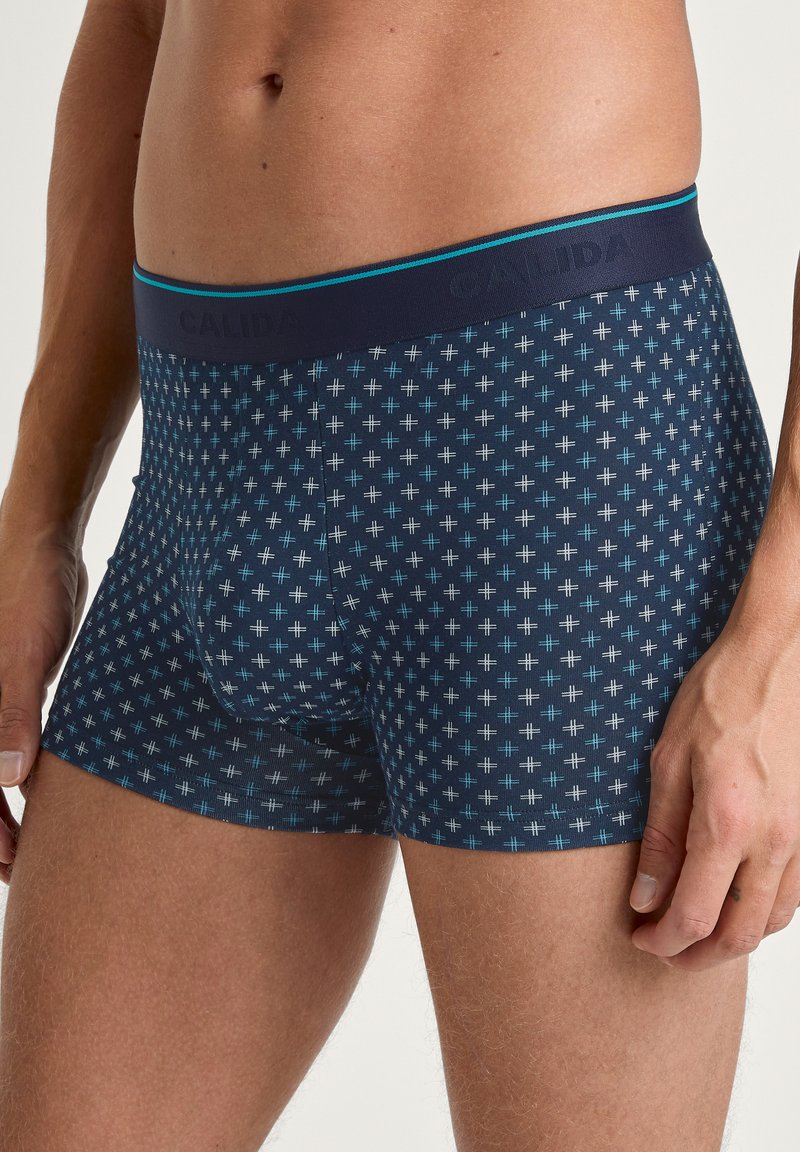 Navy blue boxers with a geometric pattern of small crosses in light blue. Features a soft waistband with CALIDA branding in dark blue.