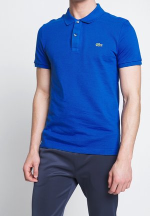 Blauw katoenen poloshirt met korte mouwen, twee knoopjes en een groen geborduurd logo op de borst. Gladde textuur, aansluitend ontwerp.