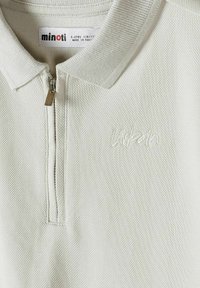Biała teksturowana koszulka polo z zamkiem błyskawicznym, haftowanym napisem „urban” na piersi oraz metką „minoti” wskazującą rozmiar 5-6 lat, wykonana w Pakistanie.