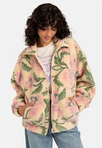 Pasztell rózsaszín és zöld virágmintás polár cipzáras dzseki, két első zsebbel és magas gallérral. Puha, texturált anyag.