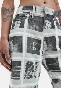Calvin Klein džinsai juodos ir baltos spalvų, su tinkleliniu raštu, turinčiu įvairius dizainus. Pagaminti iš tekstūruoto audinio su nudėvėtu apdailos efektu.