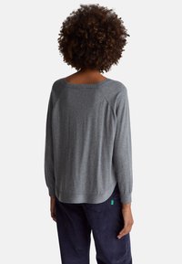 Szary sweter dziany o luźnym kroju, z rękawami raglanowymi i prążkowanym dekoltem. Wykończony zakrzywionym dołem i bocznymi rozcięciami.