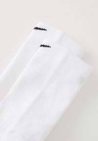 Pair of white athletic crew socks with a black swoosh logo near the cuff on a plain white background.