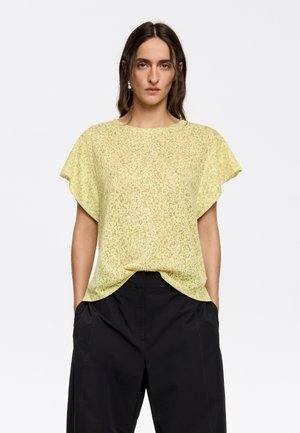 Haut jaune clair à manches courtes avec un motif texturé subtil, décolleté arrondi et coupe décontractée, associé à un pantalon large noir.