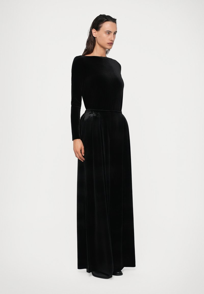 Black velvet dress with long sleeves, boat neckline, and wide, flowing skirt. Features a textured accent at the waist. Smooth, soft texture.
