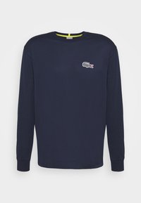 Tummansininen pitkähihainen crewneck-paita, jossa on ribbireunukset ja pieni valkoinen krokotiililogo-merkki vasemmassa rinnassa.