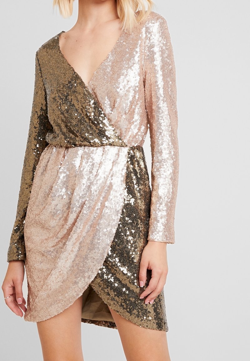 Robe enveloppante en sequins avec un décolleté en V, des manches longues et un ourlet asymétrique. Les couleurs varient du doré au rose clair. Doublure intérieure douce.
